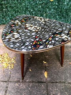 Authentique table basse tripode, de forme triangulaire, arrondie, pieds compas fuselés et embouts laiton, plateau Formica très coloré d’inspiration libre, champ doré avec liseré noir; Porte les traces du temps lui conférant tout son charme. Dimensions: H 50 cm, L 68 cm, l 62 cm.