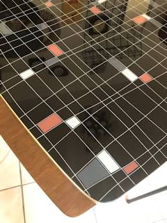 Table réglable en hauteur, deux rallonges possibles rangées sous le plateau en verre, motifs géométriques sur fond noir, pieds compas, dimensions: L 115 cm, l 65 cm, H de 65 à 75 cm modulable.