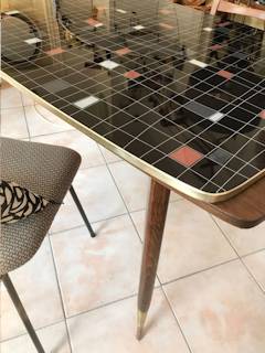 Table réglable en hauteur, deux rallonges possibles rangées sous le plateau en verre, motifs géométriques sur fond noir, pieds compas, dimensions: L 115 cm, l 65 cm, H de 65 à 75 cm modulable.