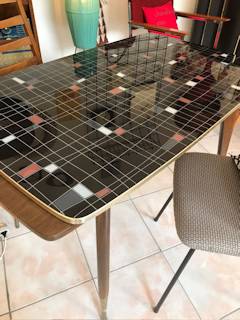Table réglable en hauteur, deux rallonges possibles rangées sous le plateau en verre, motifs géométriques sur fond noir, pieds compas, dimensions: L 115 cm, l 65 cm, H de 65 à 75 cm modulable.