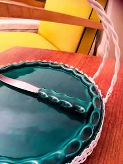 Plateau à fromage en céramique des années 50, signé Yvon Roy, avec son support en métal perforé à double anse torsadée, dans le style de Mathieu Matégot, présence de son couteau, diamètre 23,5cm, H 18,5cm.